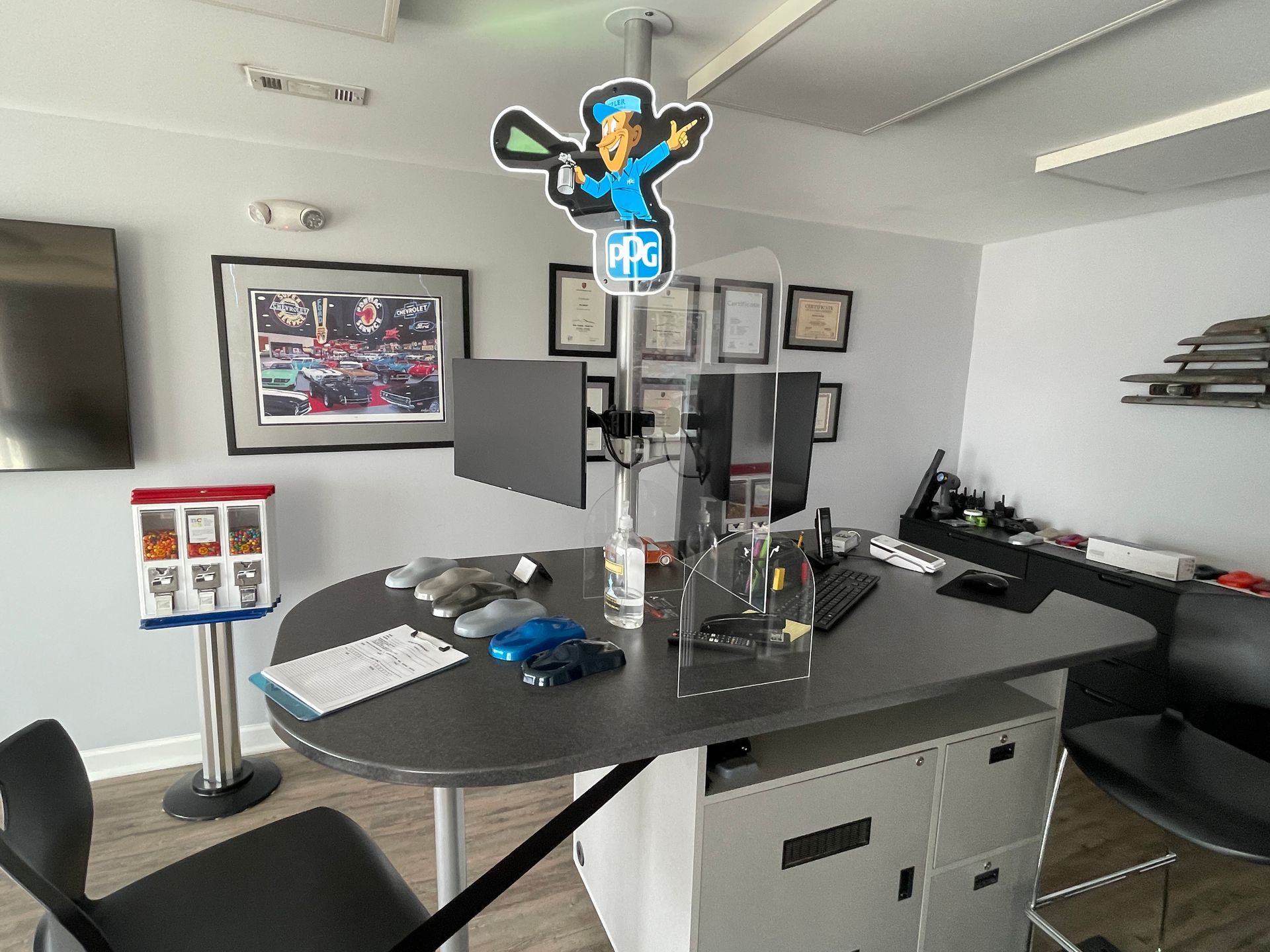 A room with a desk , chairs , computers and a gumball machine.