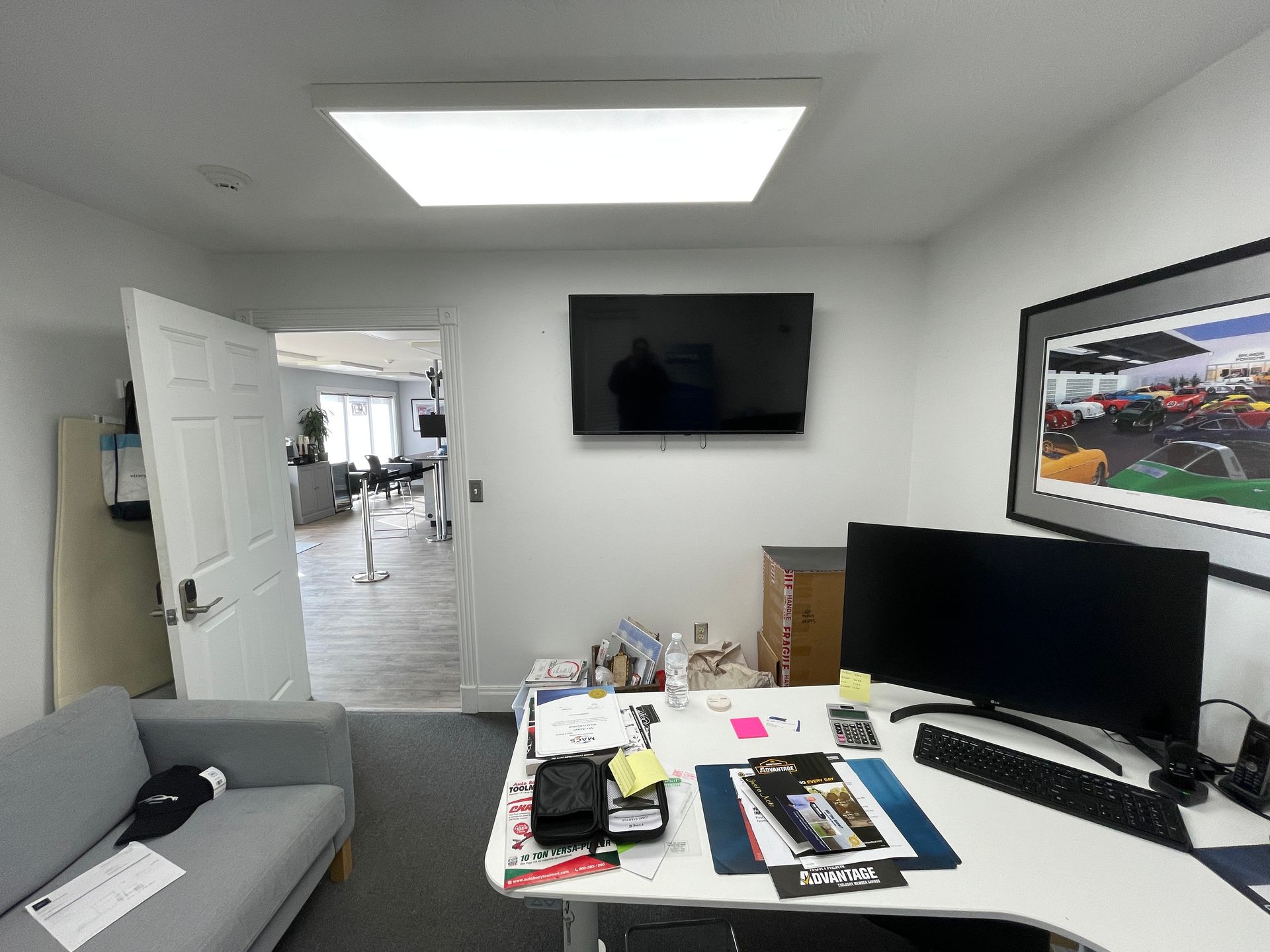 A room with a desk , two monitors , a couch and a flat screen tv.