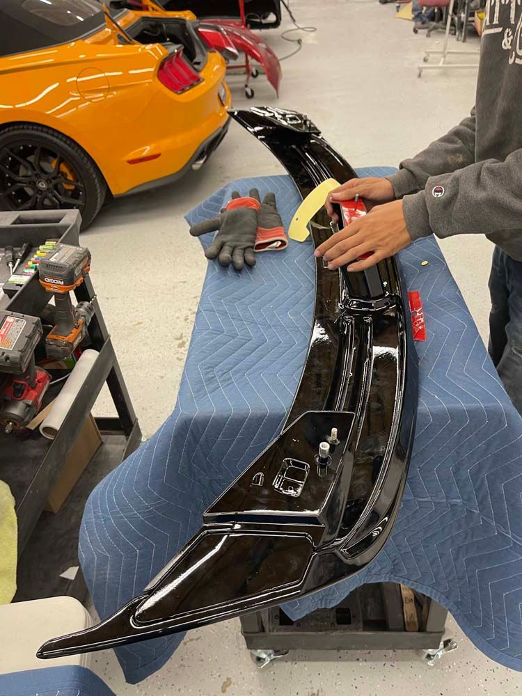 A man is working on a car with a yellow car in the background.