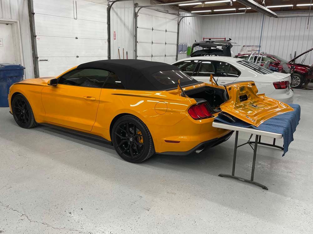 A yellow mustang convertible is parked in a garage next to a table.