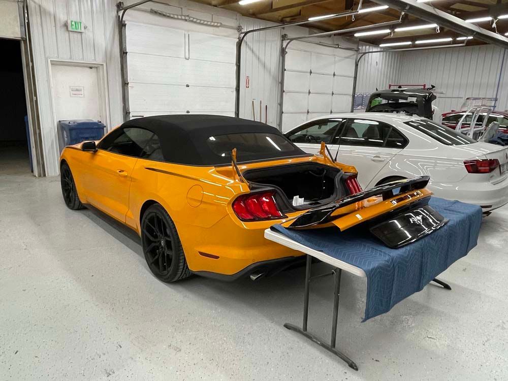 A yellow mustang convertible is parked in a garage next to a white car.