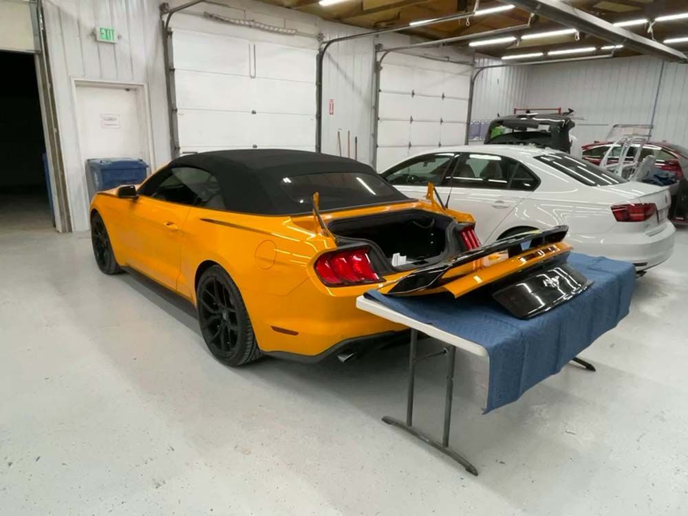A yellow mustang convertible is parked in a garage with its trunk open.