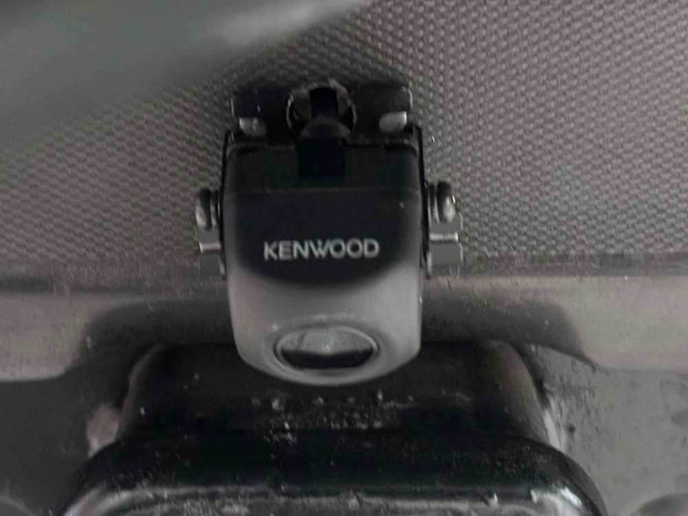 A kenwood camera is mounted to the ceiling of a car.