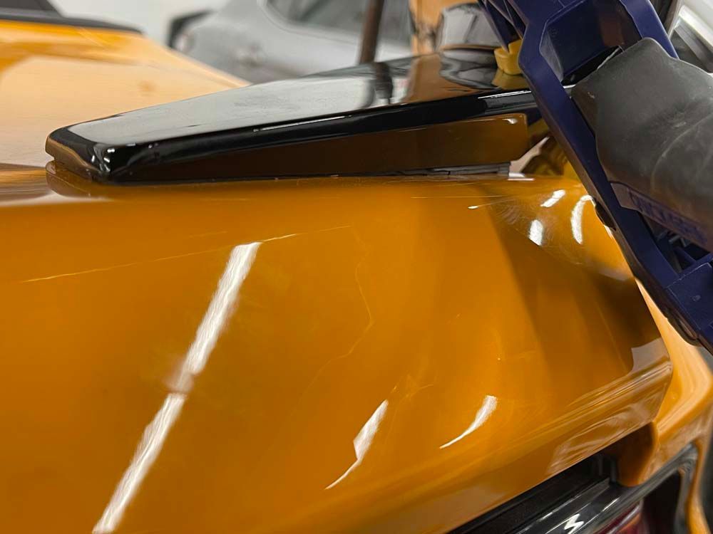 A person is holding a vacuum cleaner over a yellow car.