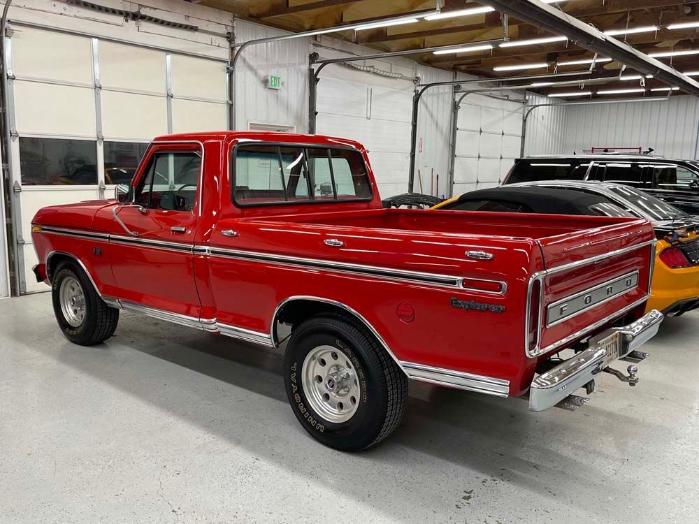 A red truck is parked in a garage next to a yellow car.