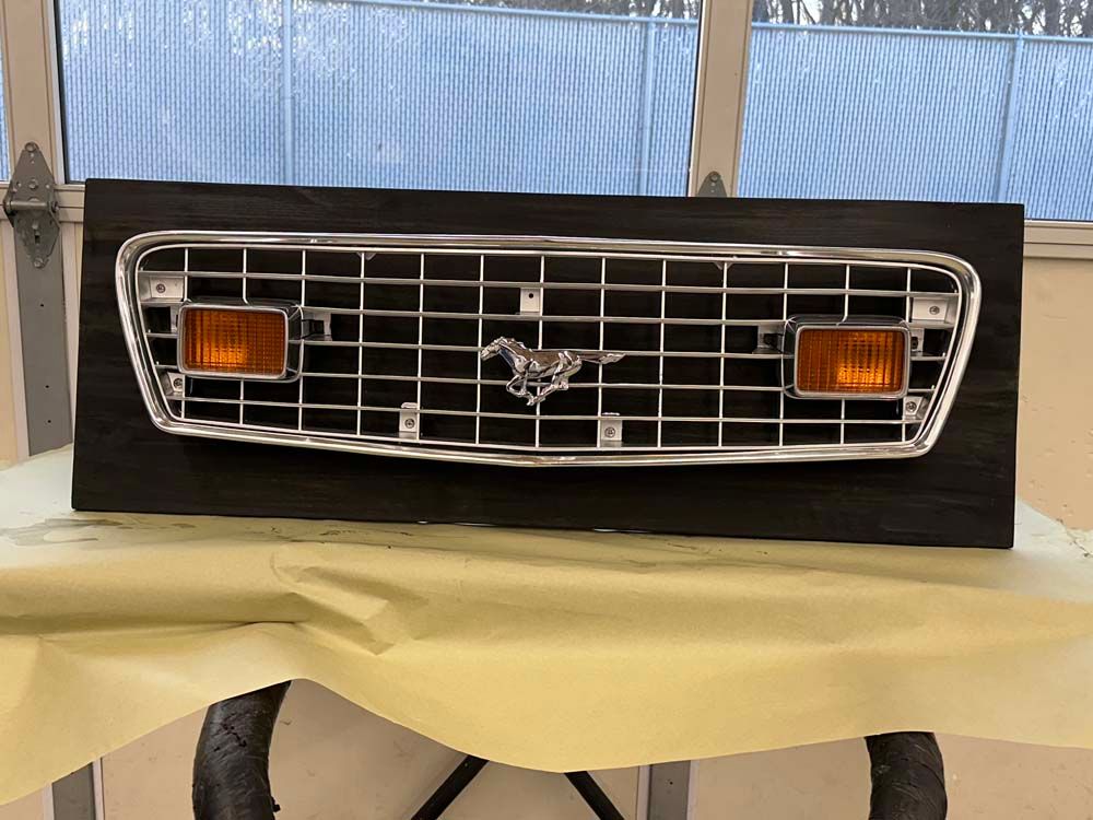 A mustang grille is displayed on a wooden board