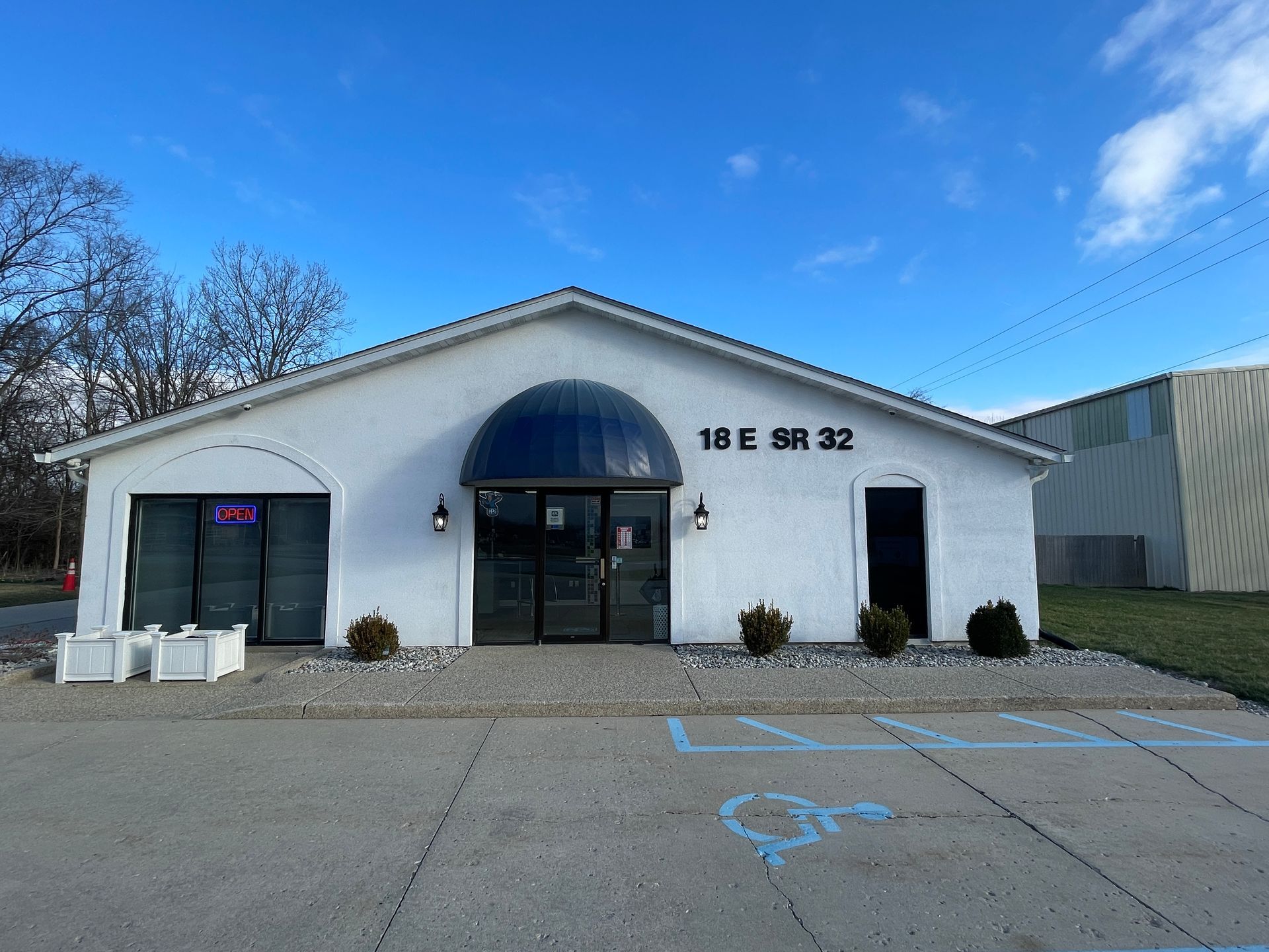 White commercial building with a blue awning, door, and the address 18 E SR 32. Accessible parking space.