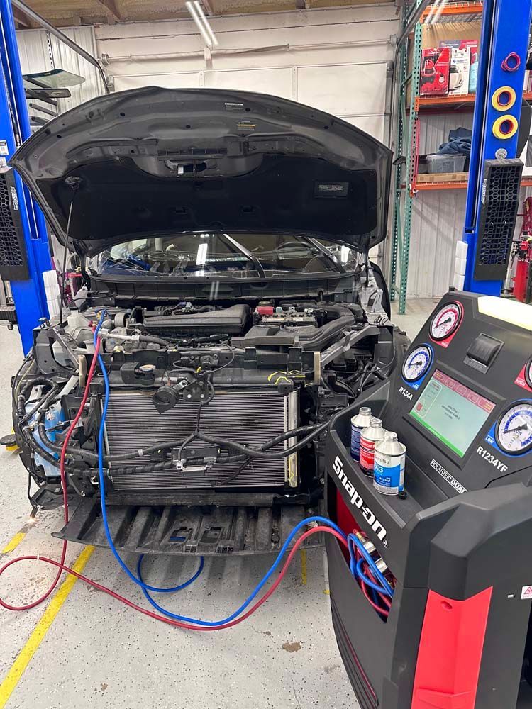 A car is being serviced in a garage with the hood up.
