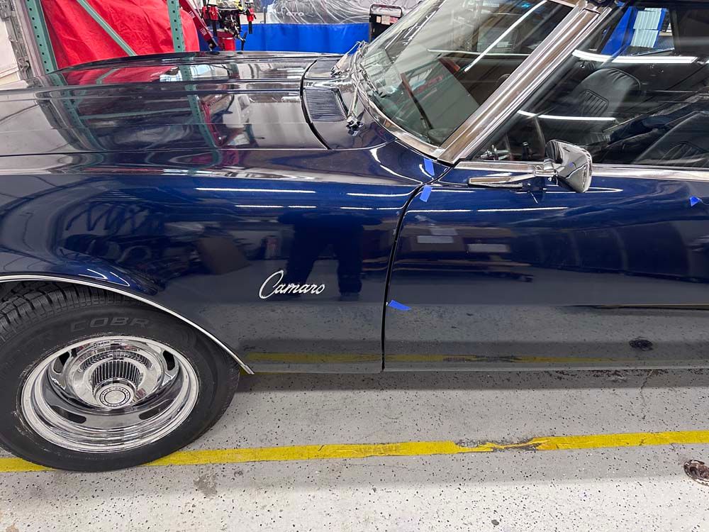 A blue car with the word camaro on the side is parked in a garage.