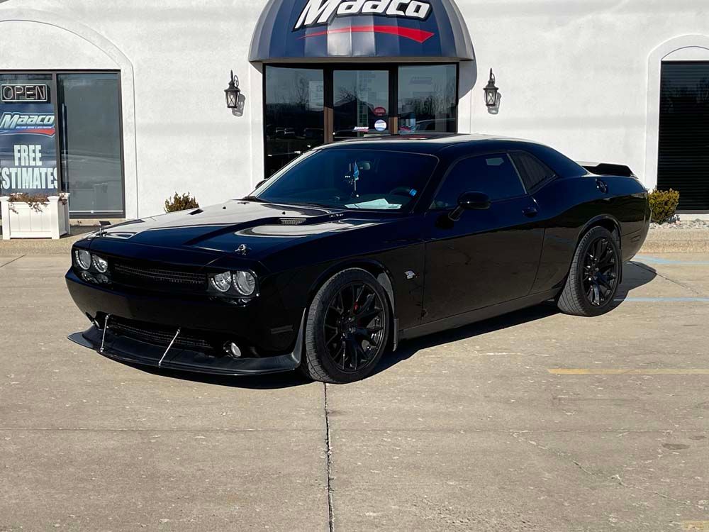 A black dodge challenger is parked in front of a modelco store