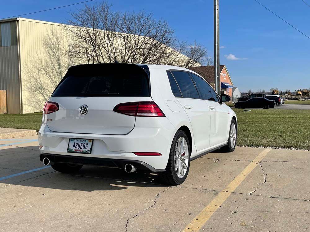 A white volkswagen golf is parked in a parking lot.