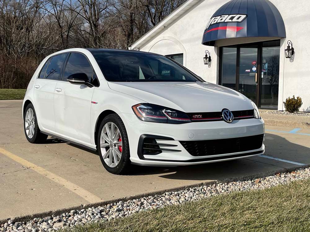 A white volkswagen golf gti is parked in front of a car dealership.