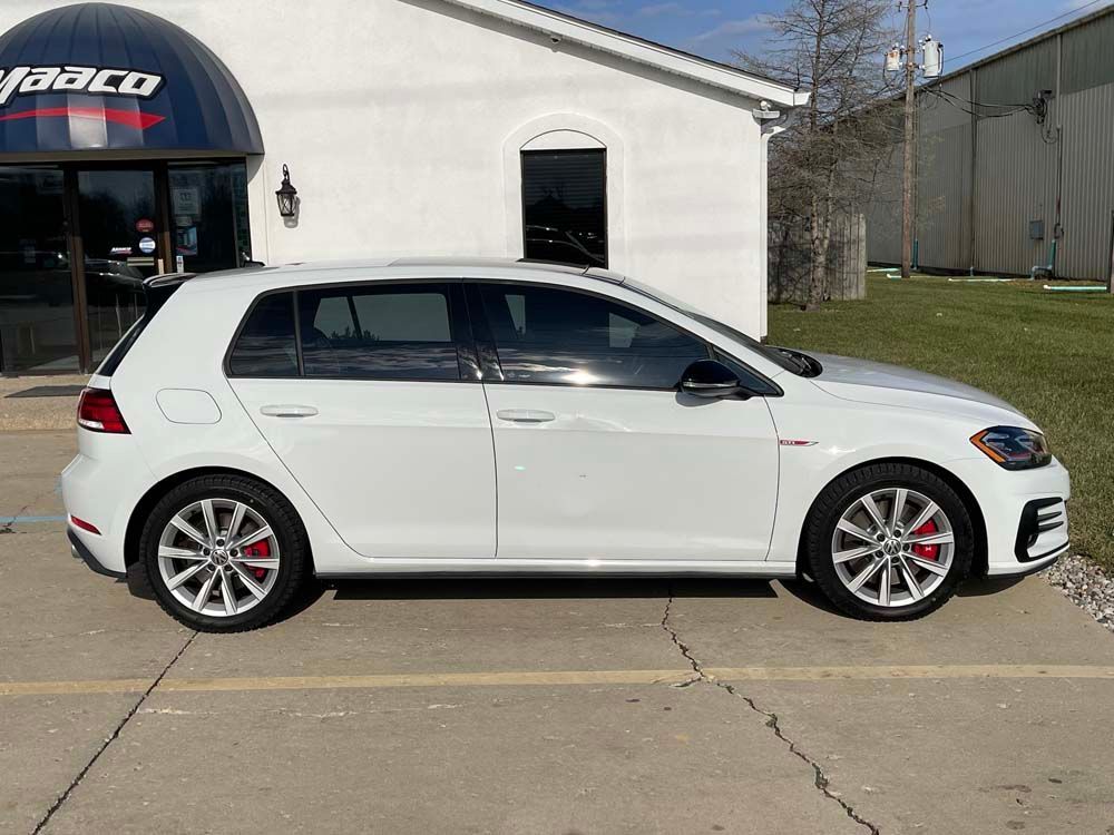 A white volkswagen golf gti is parked in front of a building.