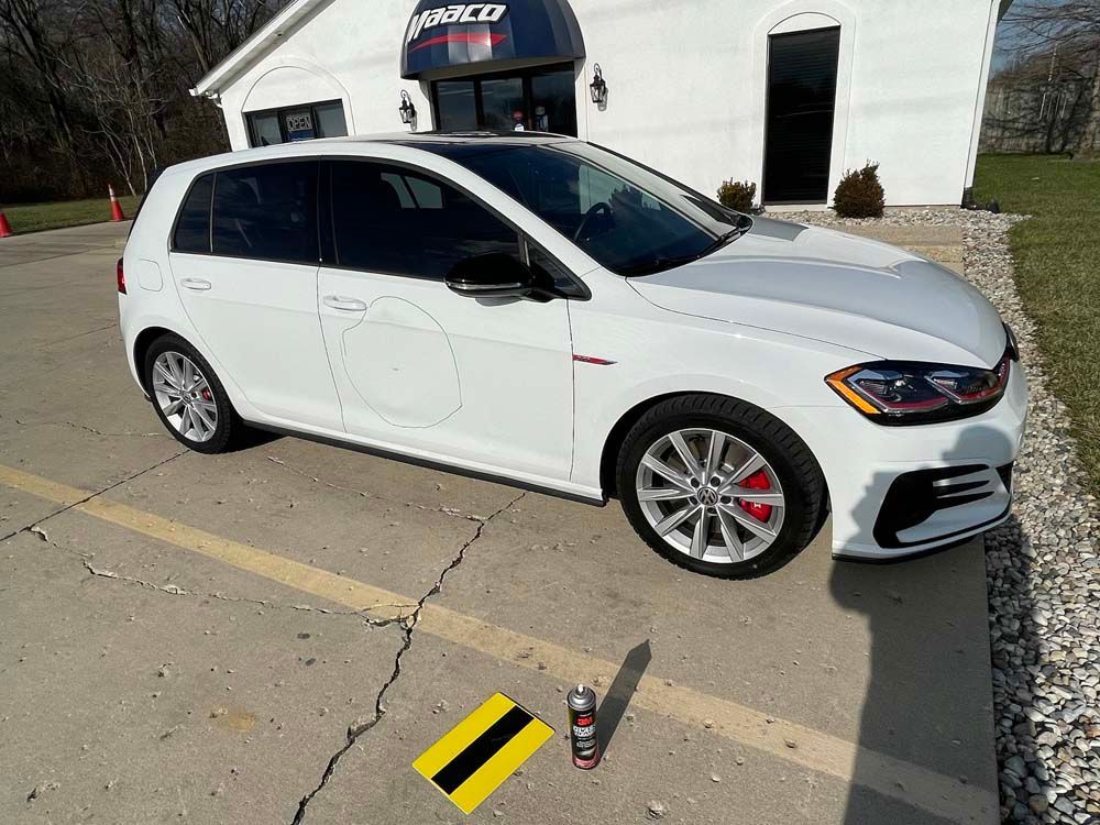 A white car is parked in a parking lot in front of a building.