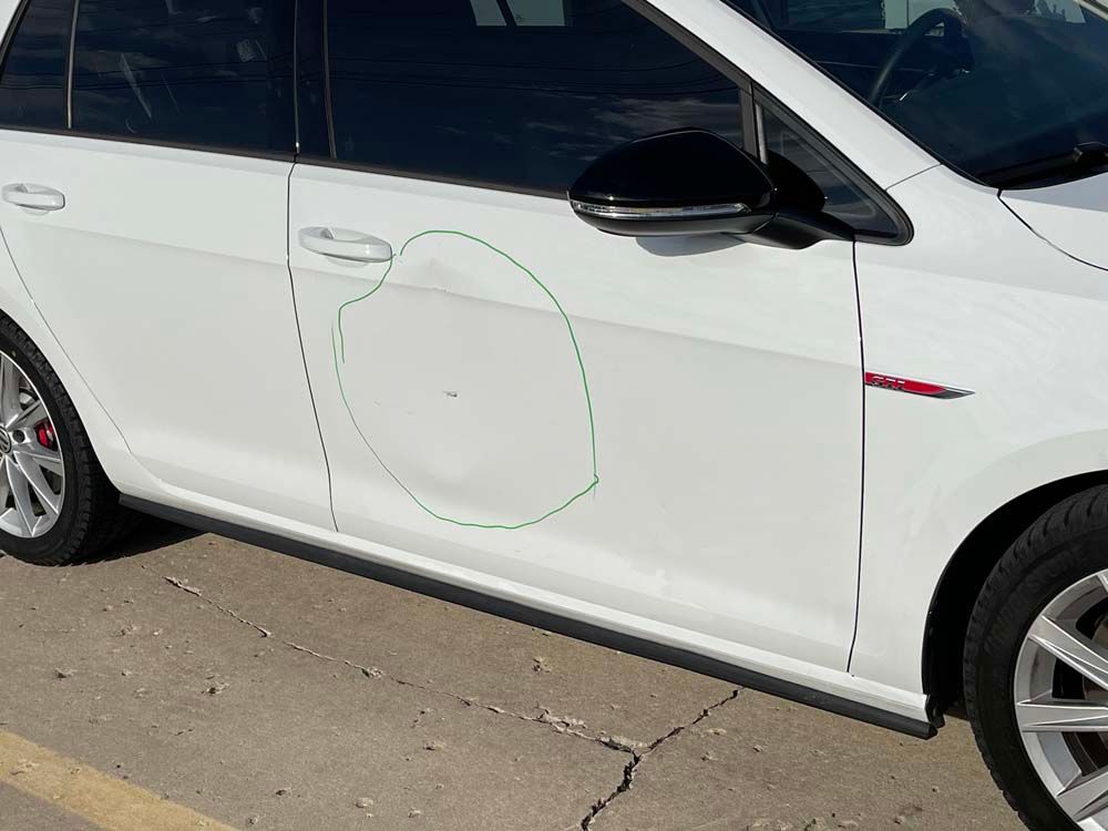 A white car with a damaged door is parked in a parking lot.