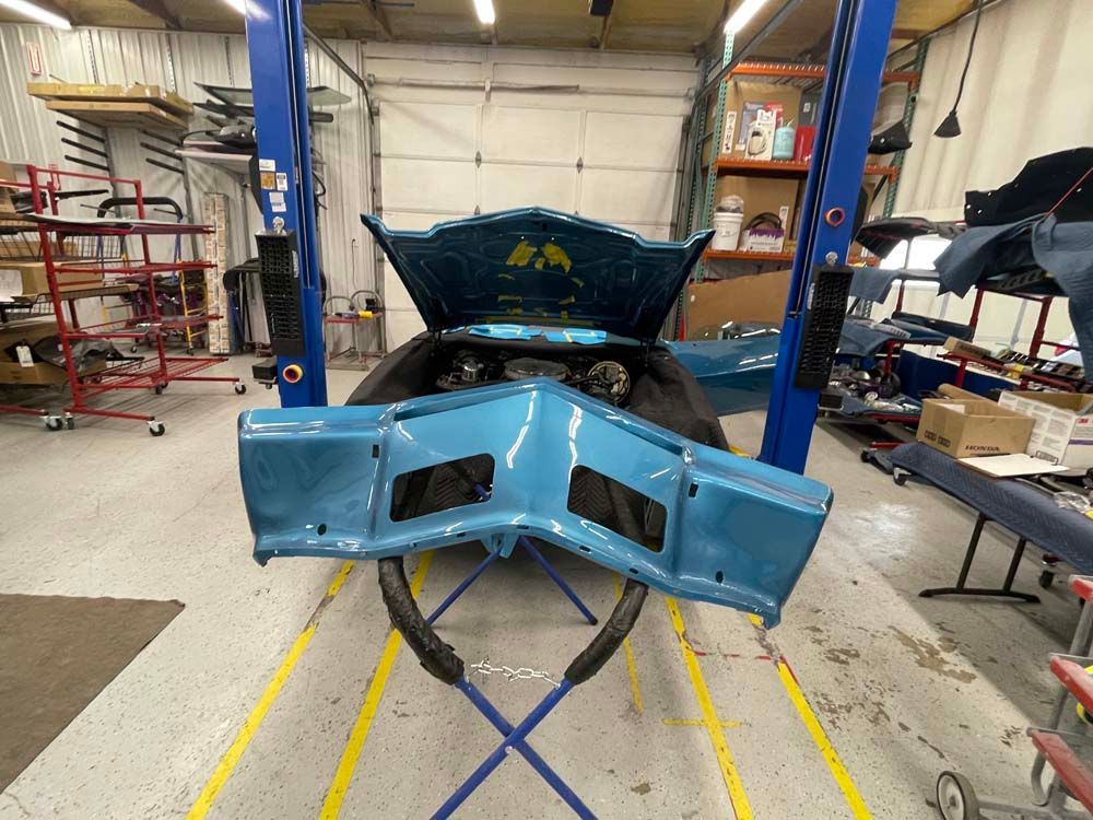 A blue car with the hood open is on a lift in a garage.