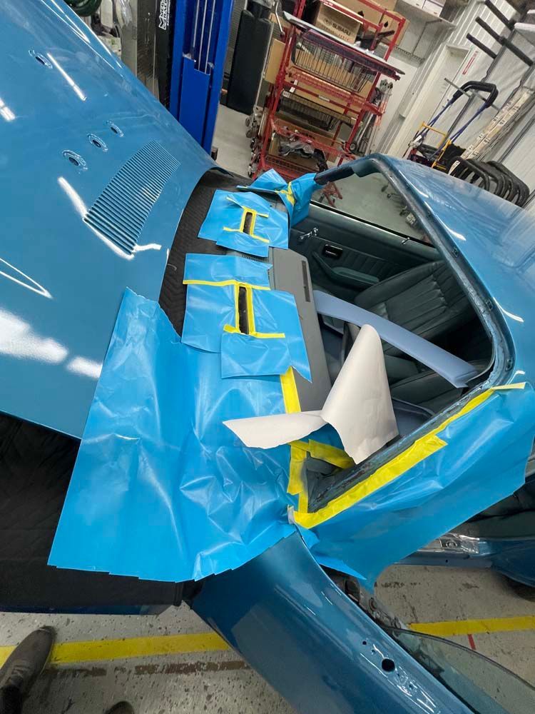 A blue car is wrapped in blue tape in a garage.