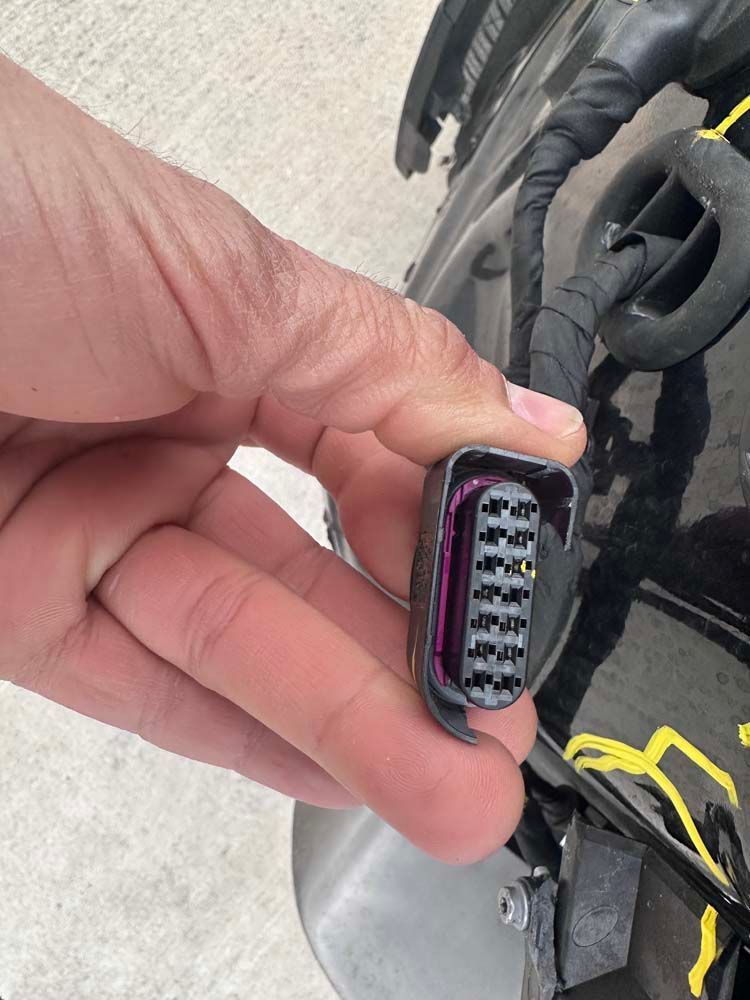 A person is holding a connector in their hand in front of a car.