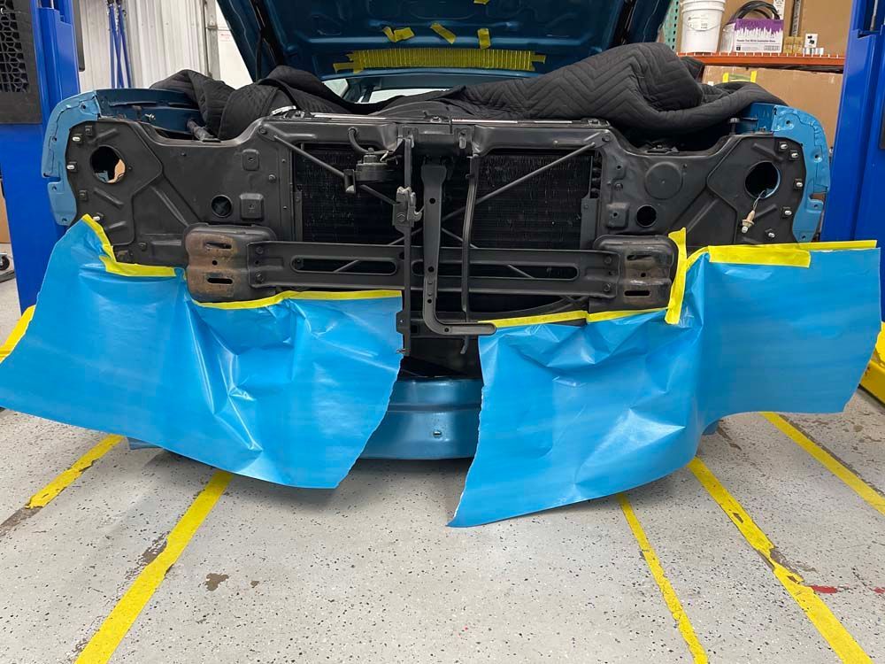 The front end of a car is covered in blue tape
