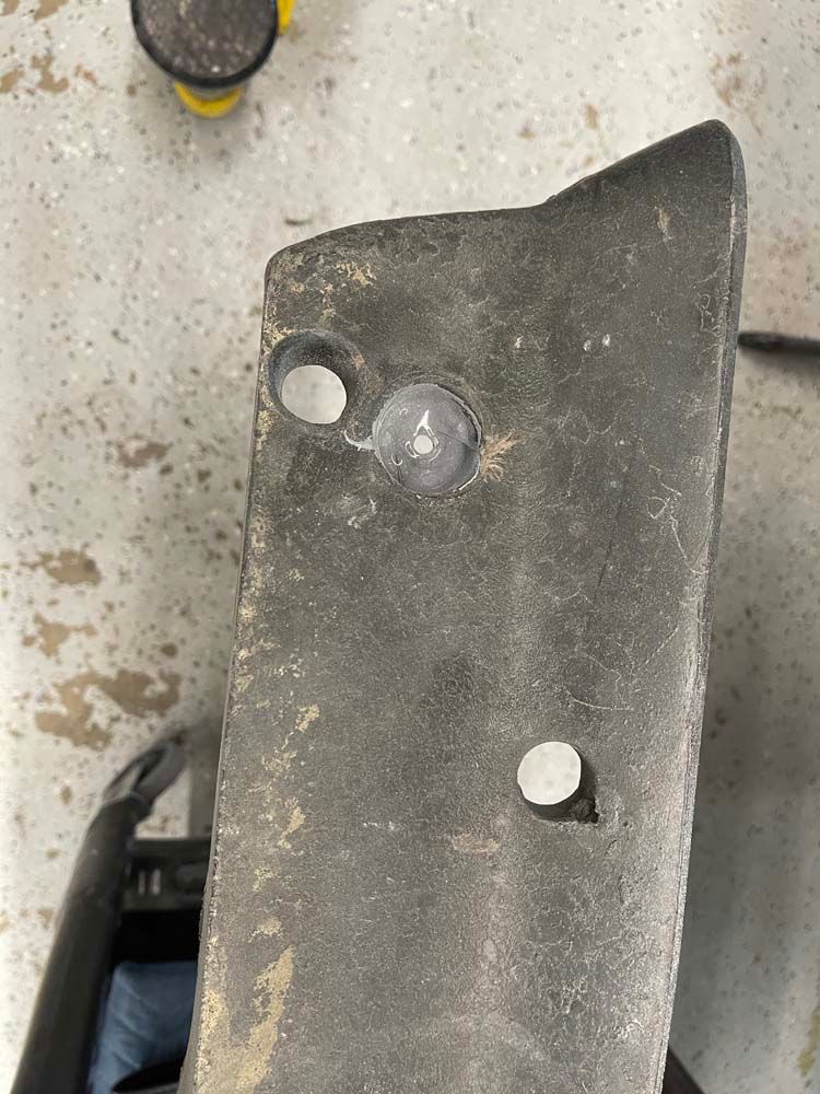 A piece of metal with two holes in it is sitting on the floor.