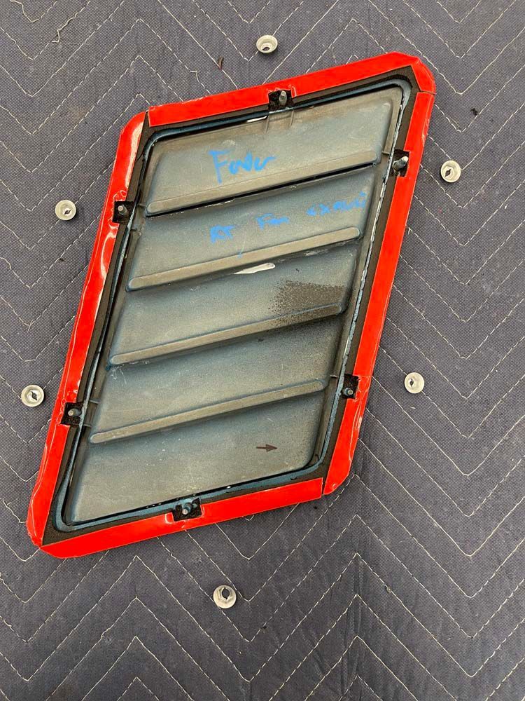 A red hood scoop is sitting on top of a gray blanket.