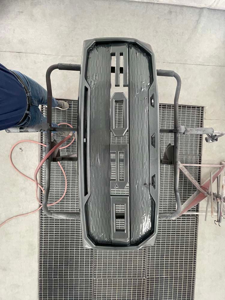 A ford grille is being painted in a garage.