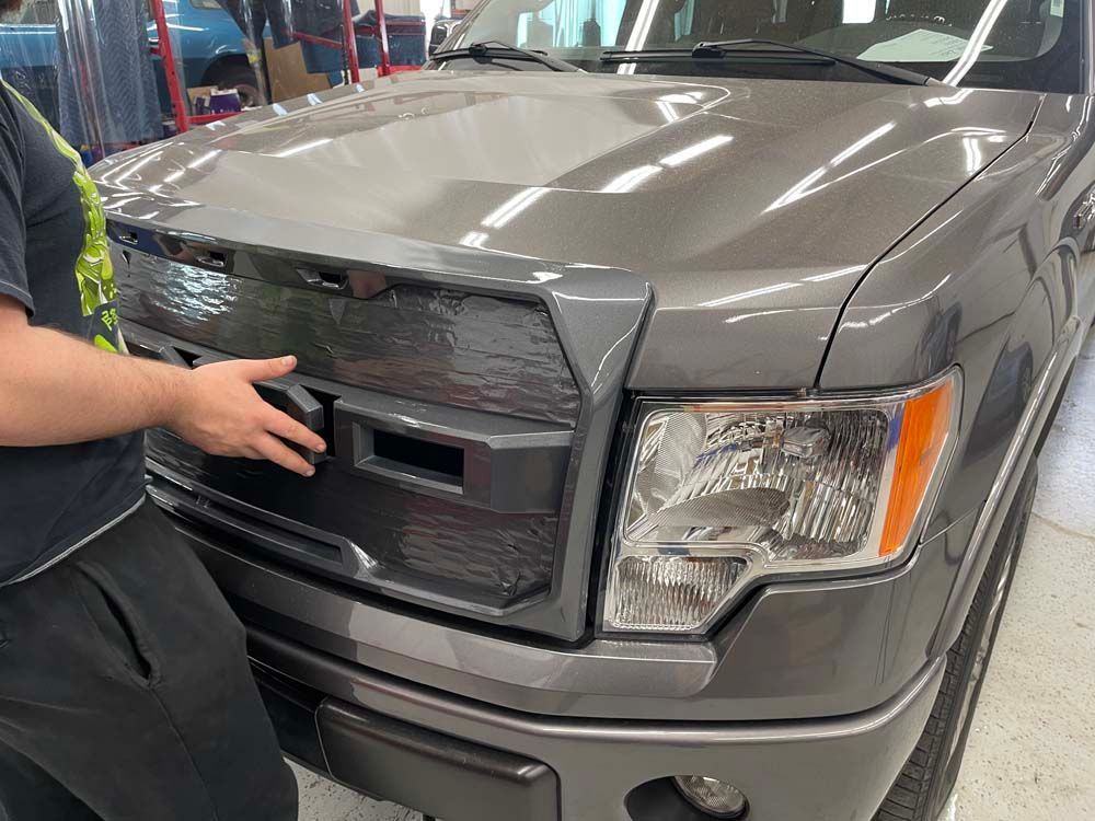 A man is standing next to a gray truck in a garage.