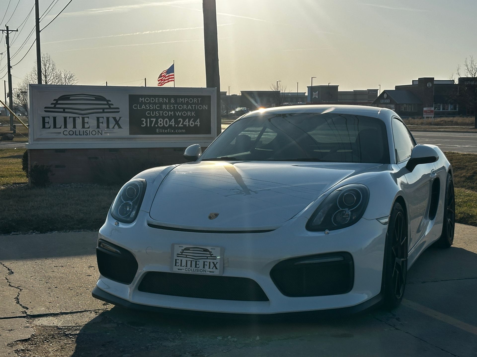 White Porsche sports car parked in front of a business sign, sunny outdoor setting.