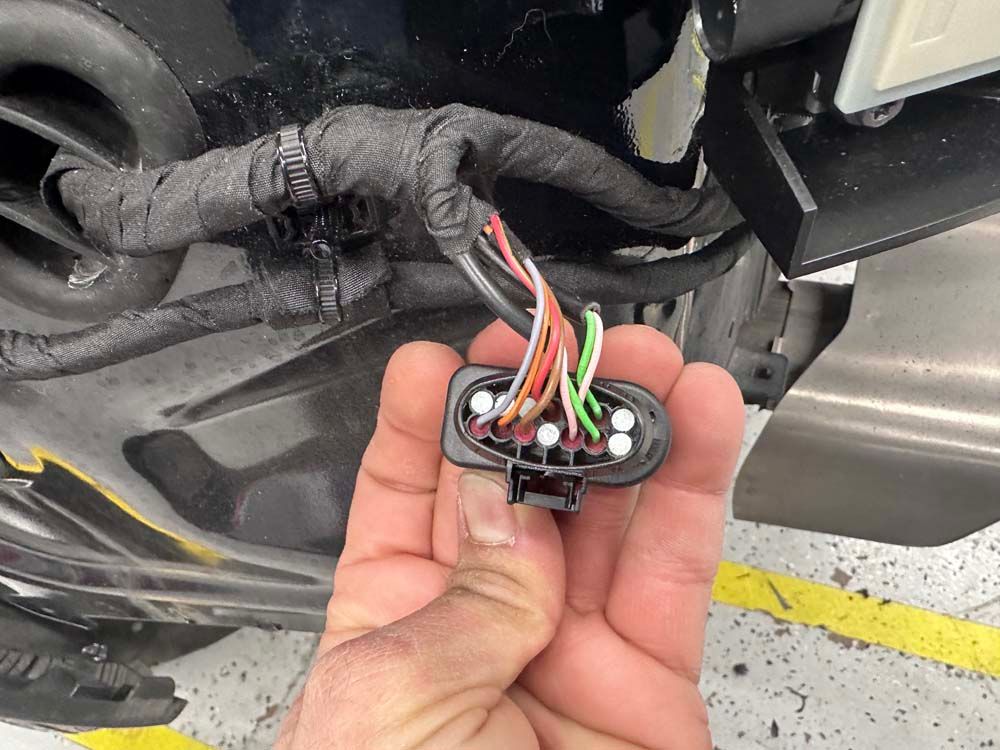 A person is holding a connector in their hand in front of a car.