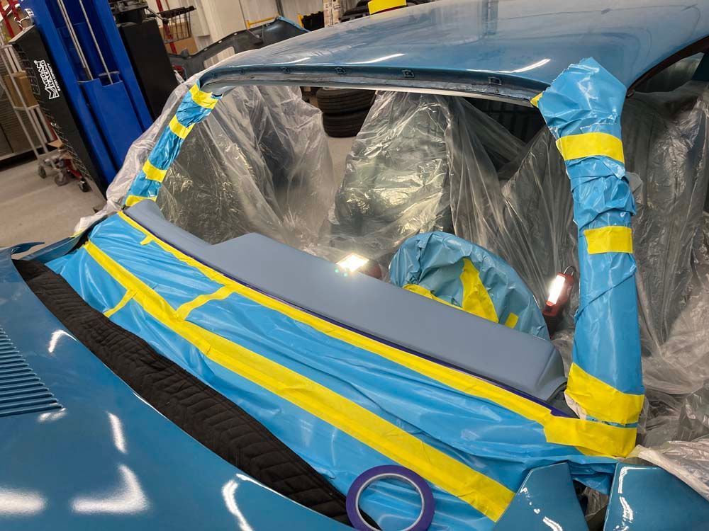 A blue car is covered in plastic wrap and tape.
