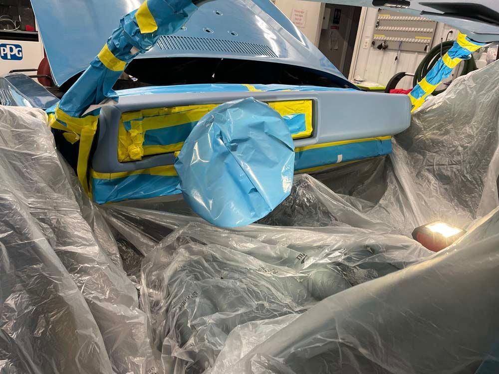 A car is covered in plastic while being painted in a garage.