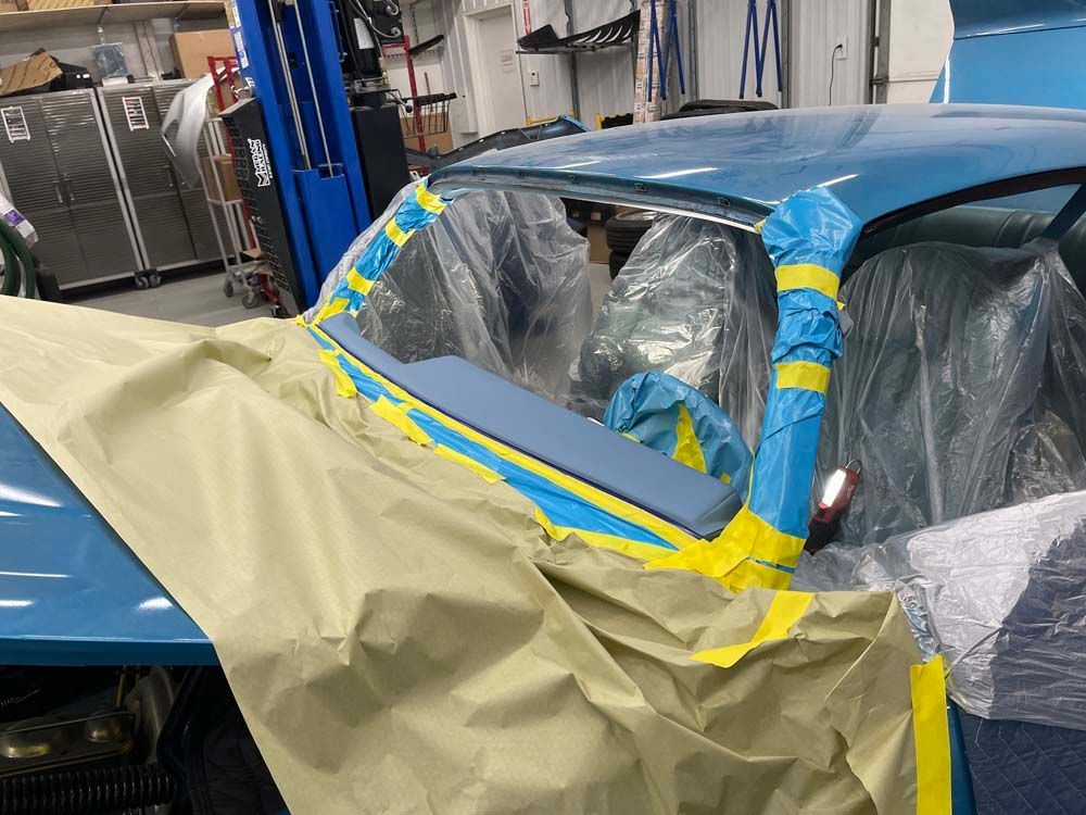 A blue car is being painted in a garage.