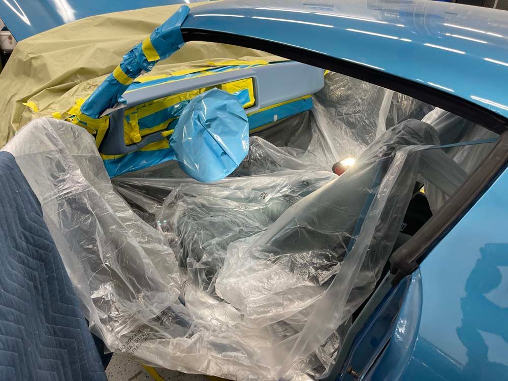 A blue car is covered in plastic while being painted.