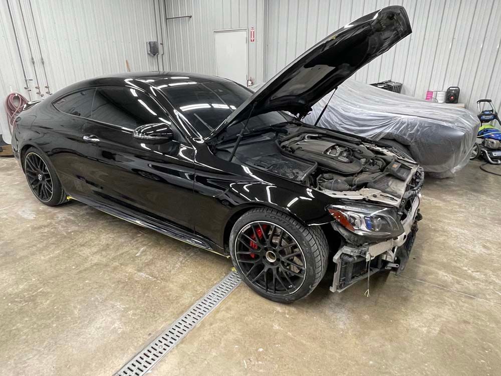 A black car with the hood up is parked in a garage.