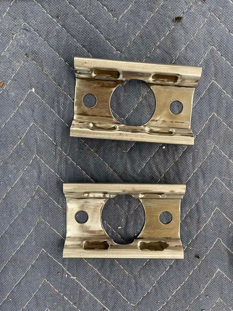 A pair of metal brackets with holes in them are sitting on top of a quilt.