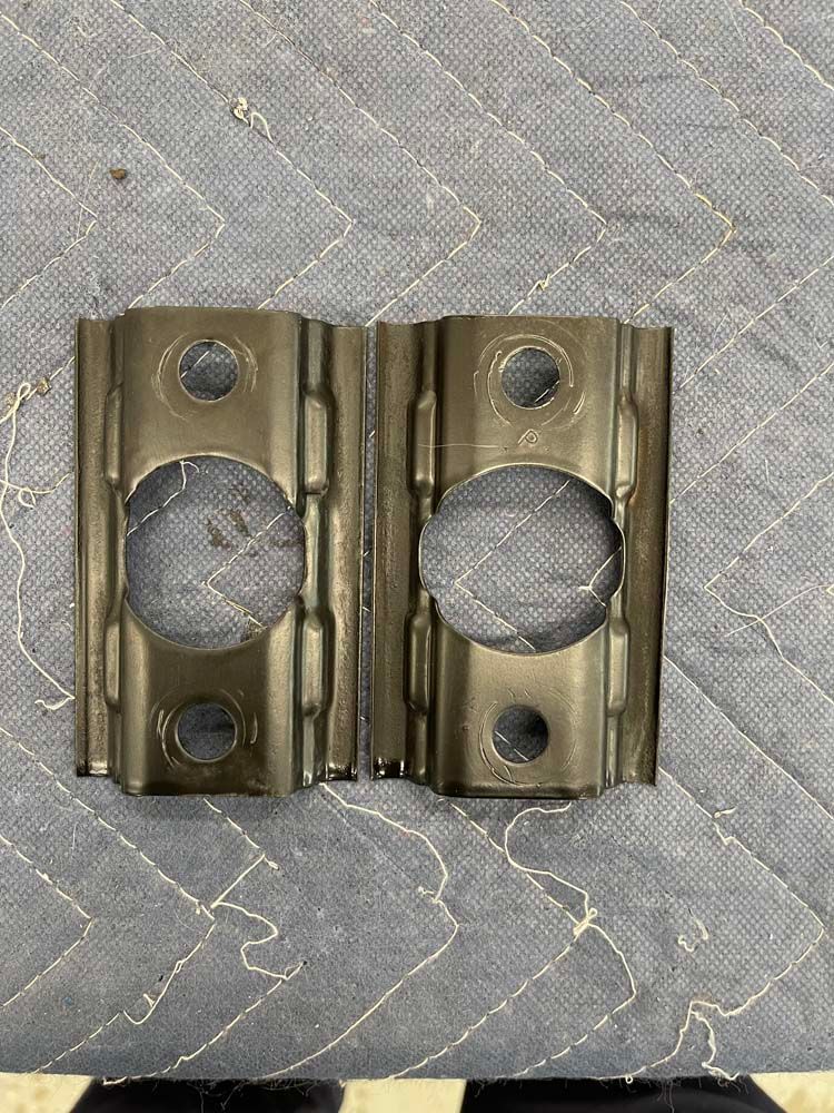 A pair of metal brackets with holes in them are sitting on top of a quilt.