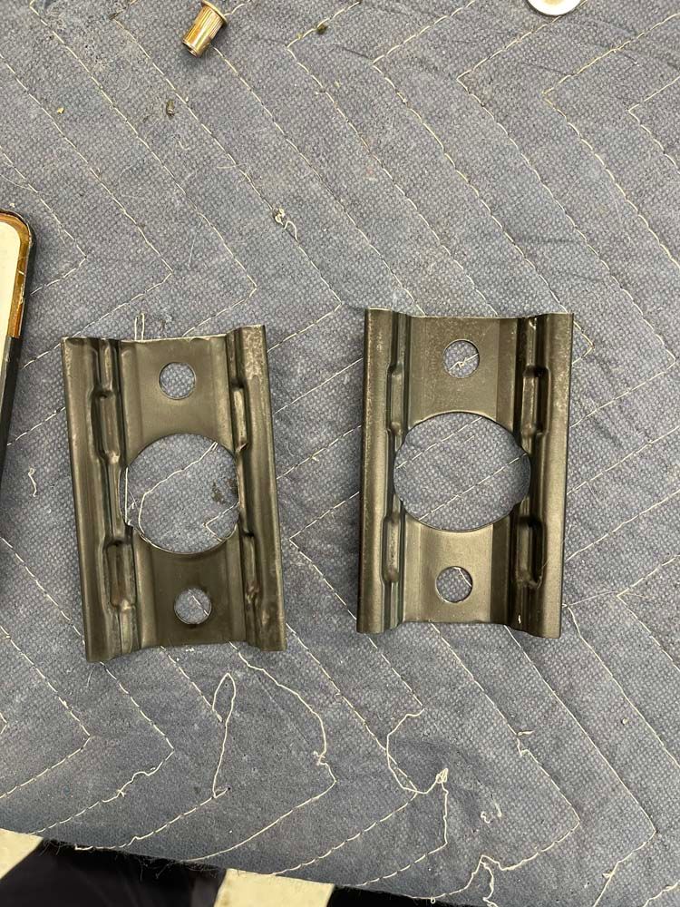 Two metal pieces with holes in them are sitting on top of a quilted table.