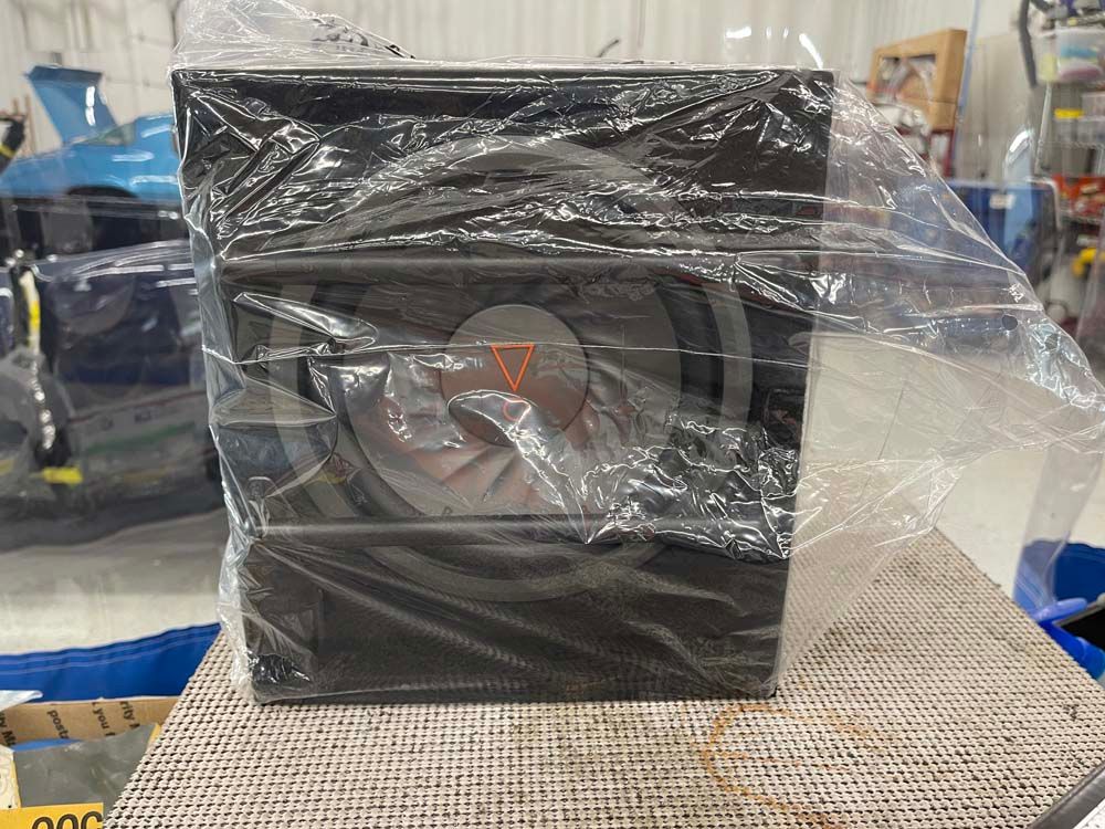 A subwoofer is wrapped in plastic and sitting on a table.