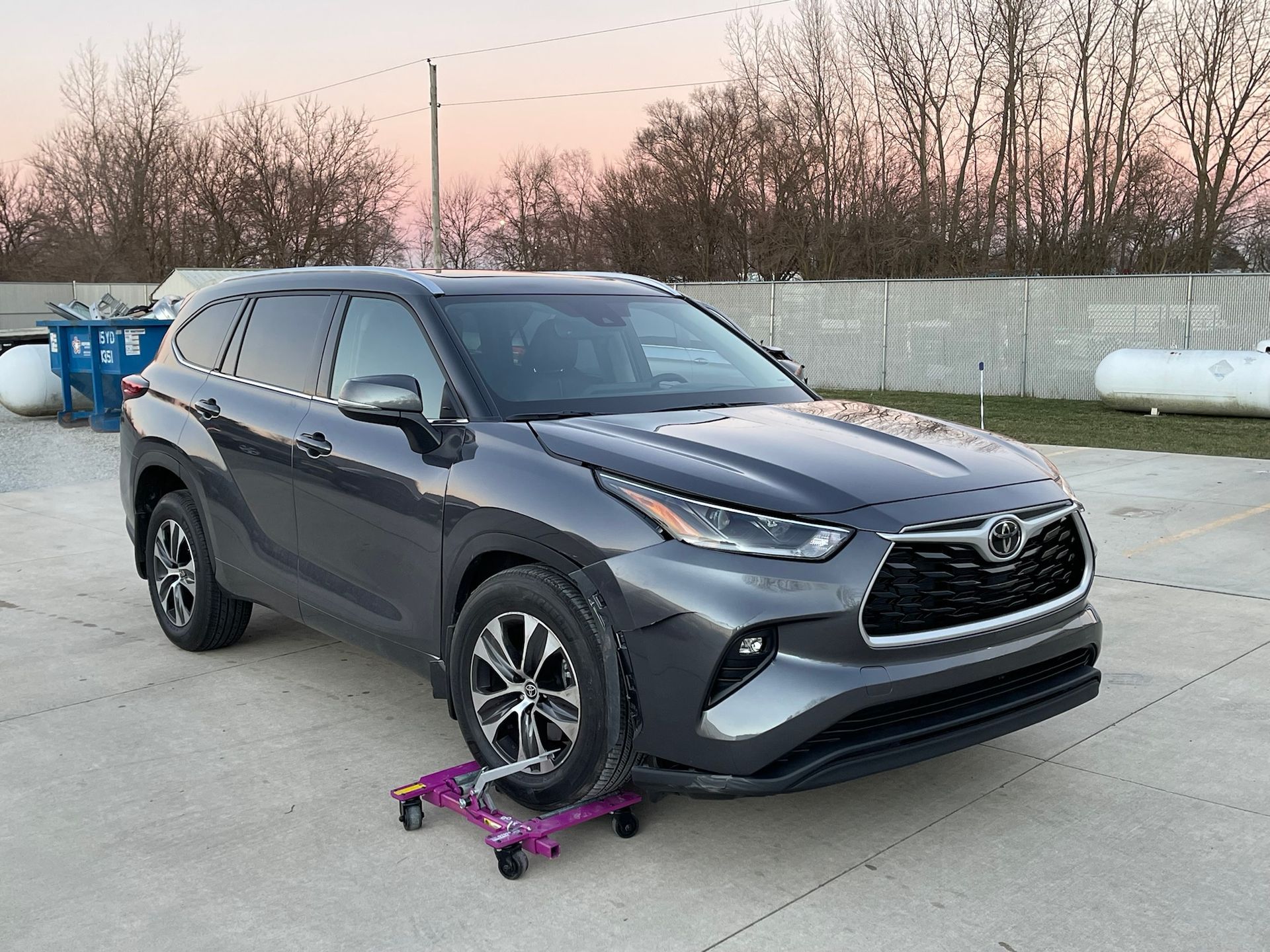 A toyota highlander is parked in a parking lot with a tire on a dolly.