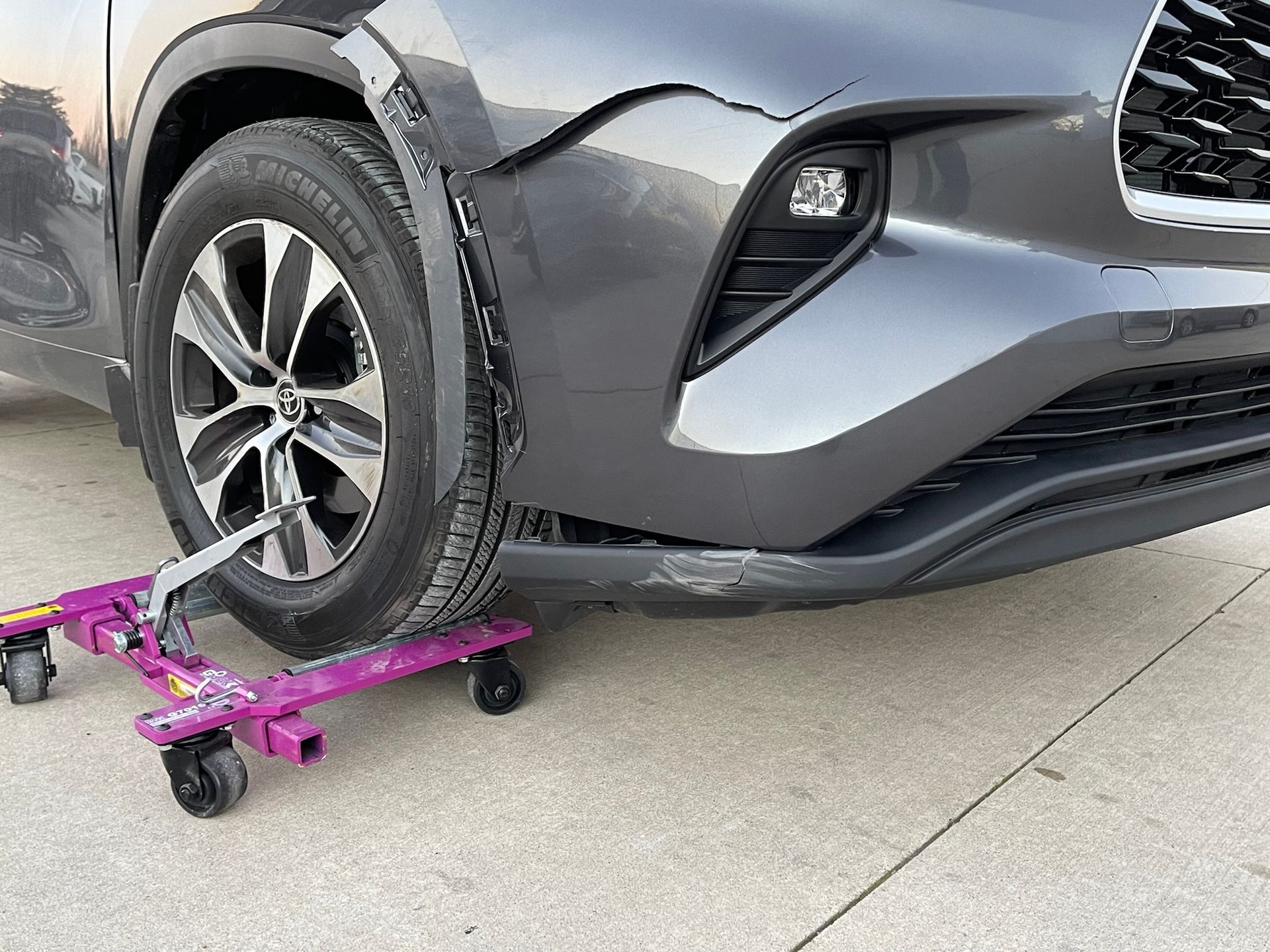 A gray car is sitting on a purple wheel dolly.