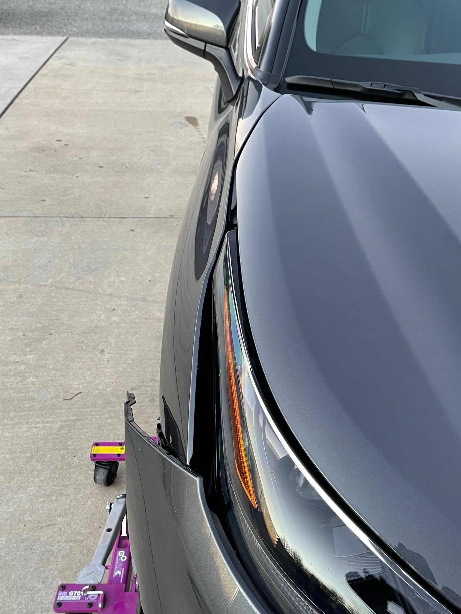 A black car with a damaged front bumper is parked on the side of the road.