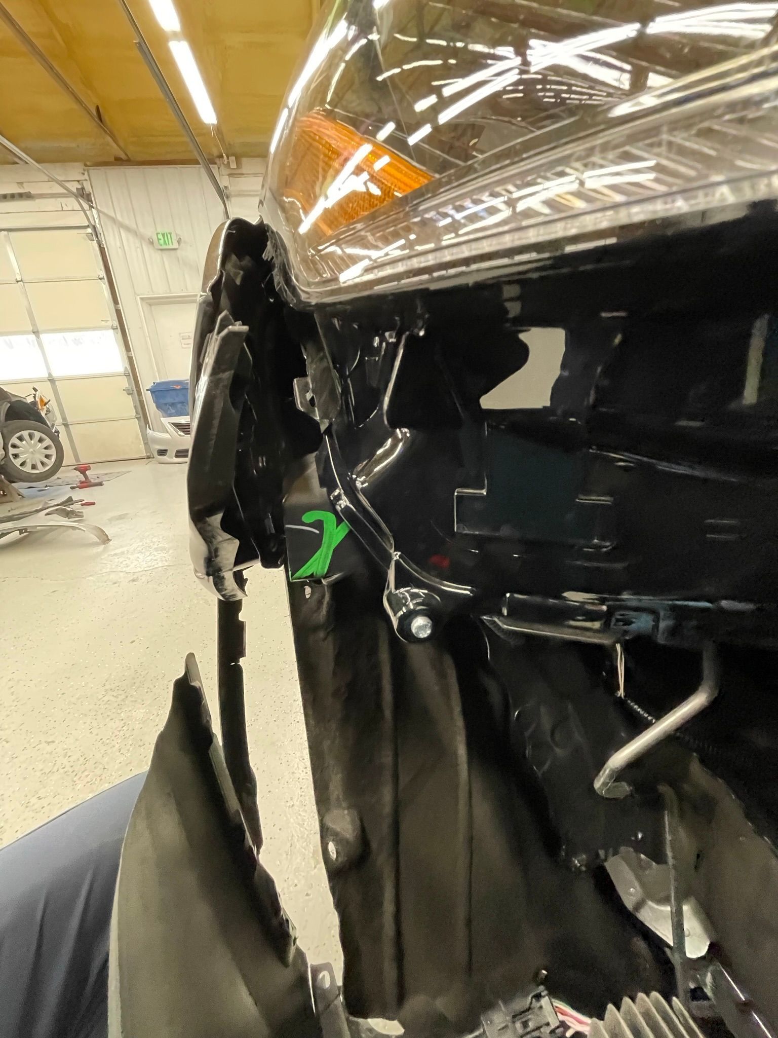 A car is being repaired in a garage and the front bumper is being removed.