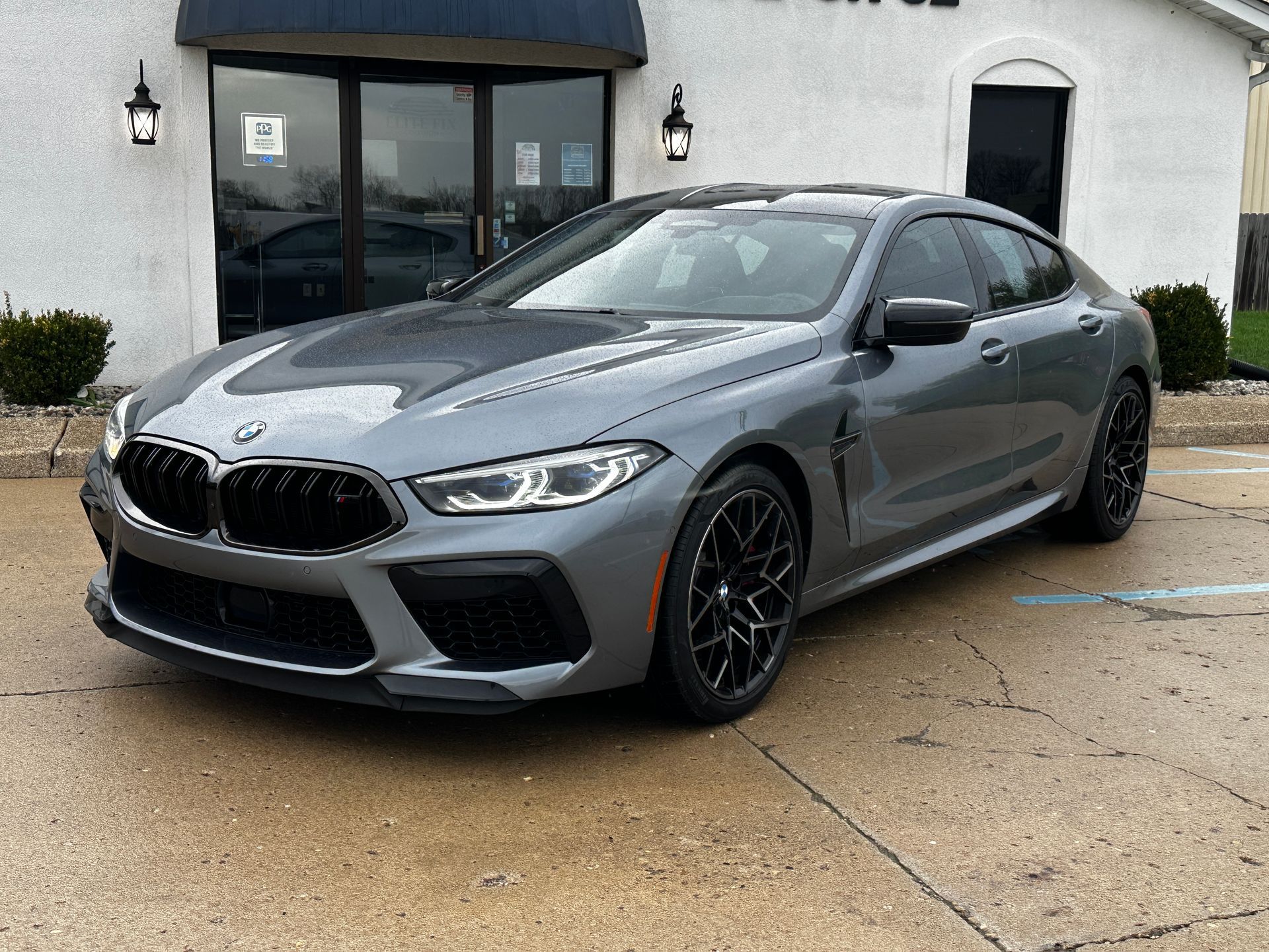 Gray BMW M8 Gran Coupe parked in front of a building with black trim and windows.