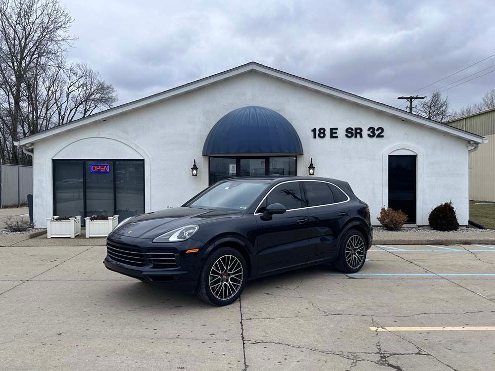 A black porsche cayenne is parked in front of a white building.