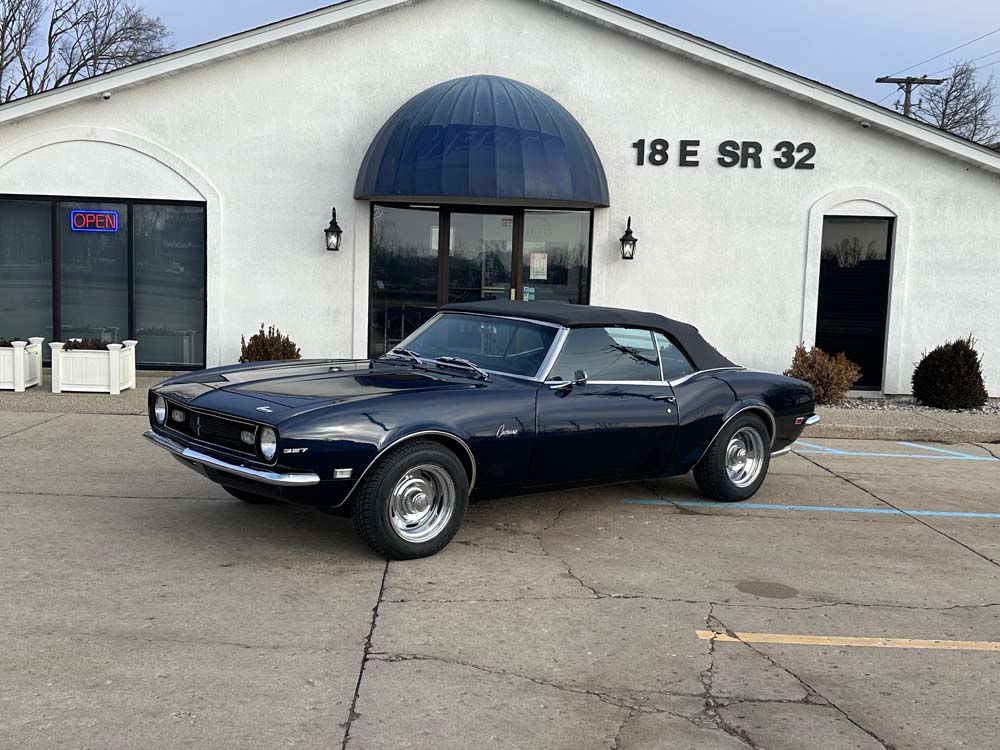 A blue car is parked in front of a white building.