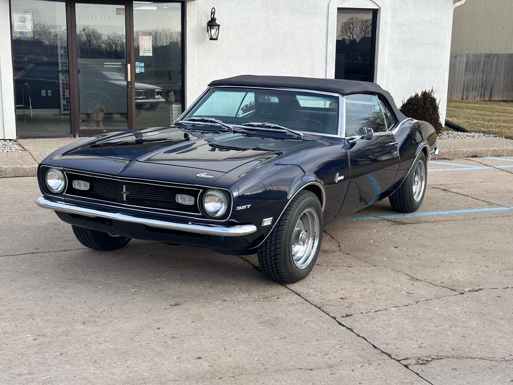 Dark blue convertible classic car parked in front of a building.