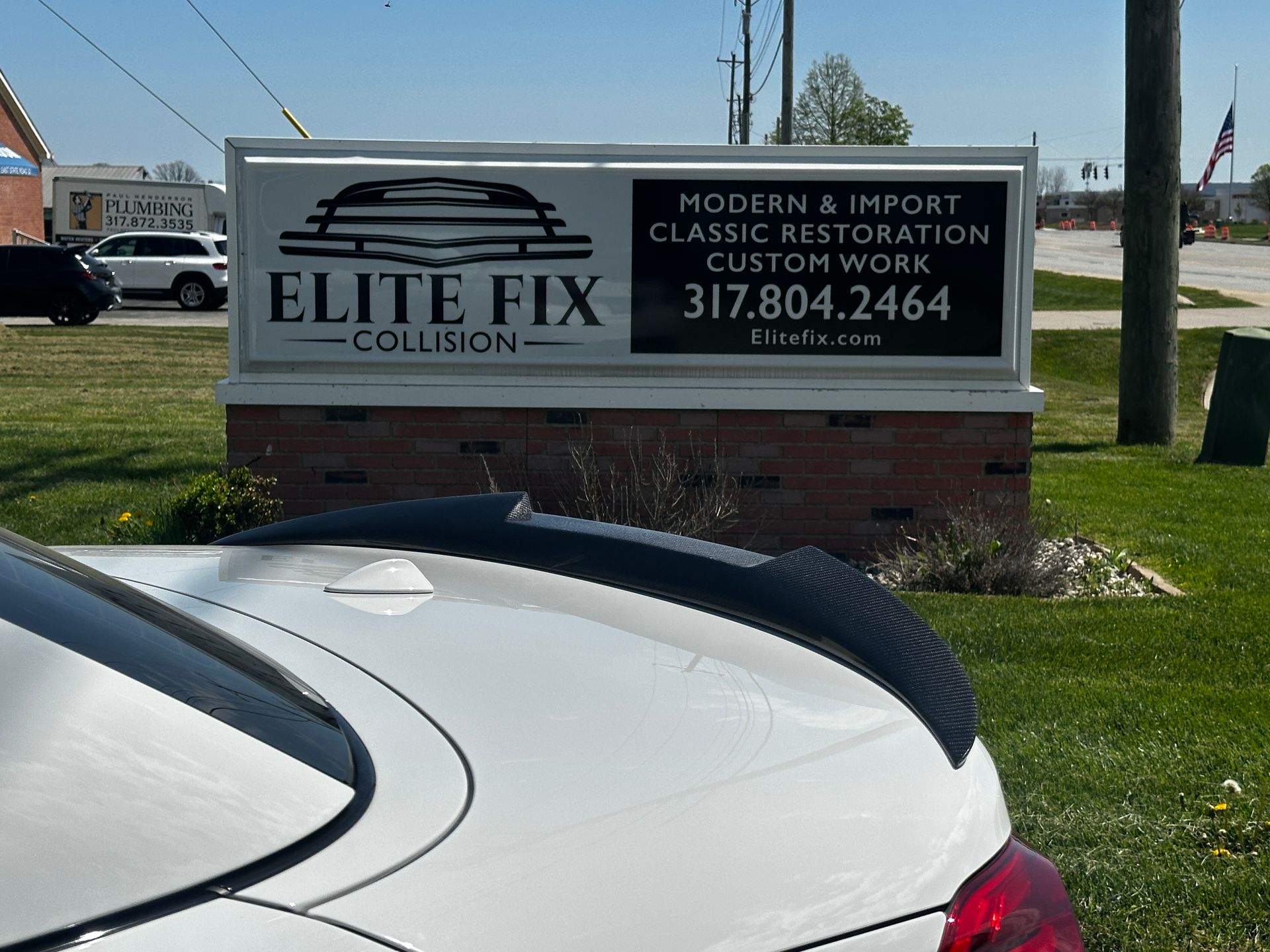 White car in front of a sign for Elite Fix Collision, which provides car restoration services.