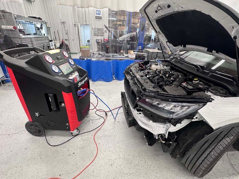 A car is being serviced in a garage with the hood open.