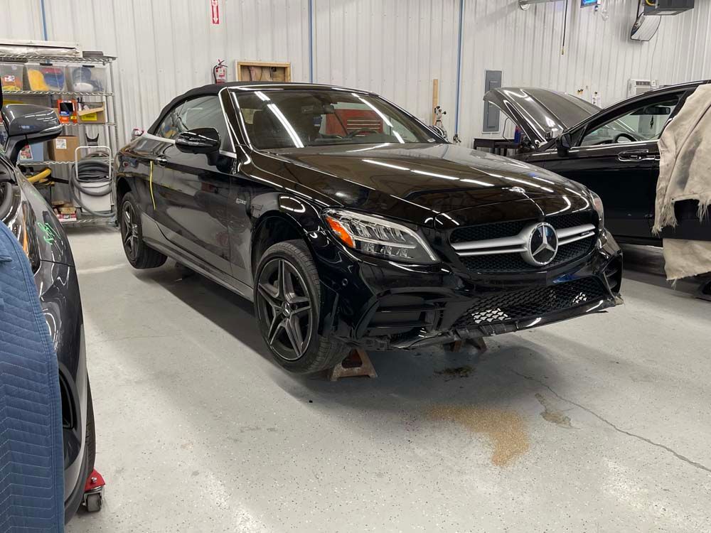 A black mercedes benz is sitting on a jack in a garage.