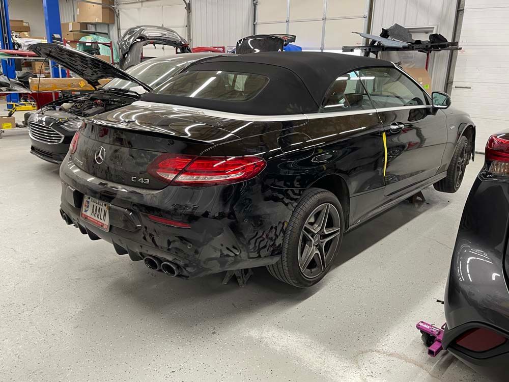 A black convertible is parked in a garage with its hood up.